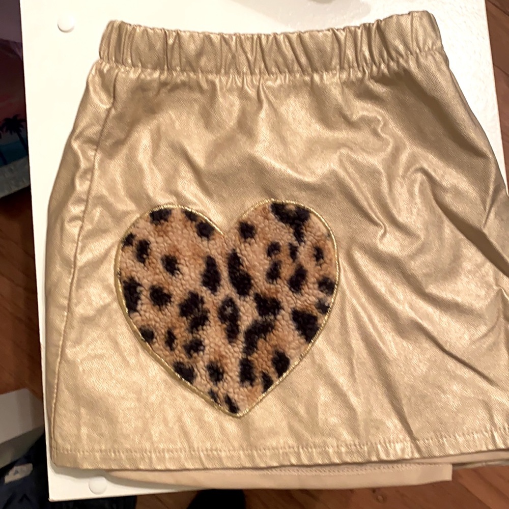 Mini skirt. Metallic gold, faux leather, with a faux fur leopard print heart.